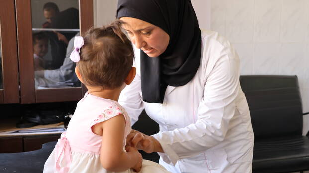 Eine Gesundheitshelferin in unseren mobilen Kliniken in Syrien untersucht ein Kleinkind.
