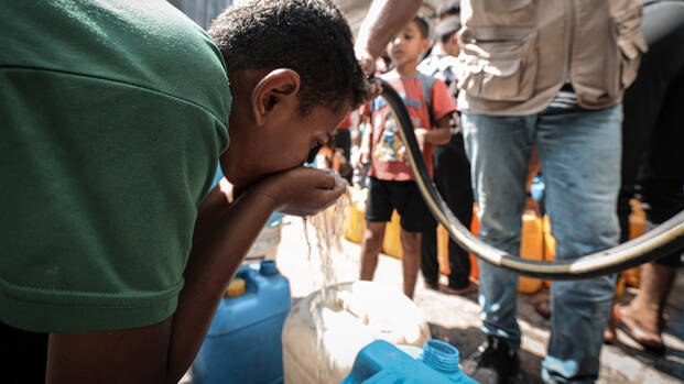 Ein Kind trinkt im Norden Gazas frisches Wasser aus einem Schlauch, den ein Mitarbeiter von Aktion gegen den Hunger hält.