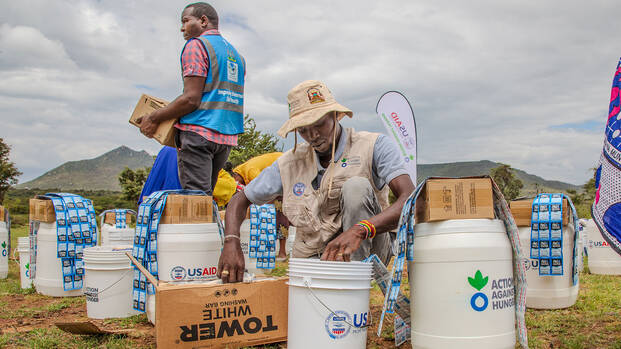 Einer unserer Mitarbeiter in Kenia füllt Hilfsgüter in Eimer mit der Aufschrift "Aktion gegen den Hunger" und "USAID".