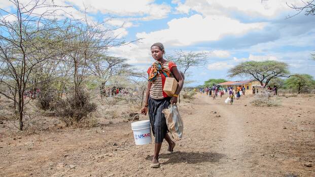 Eine Frau trägt einen Wasserkanister mit der Aufschrift "USAID".