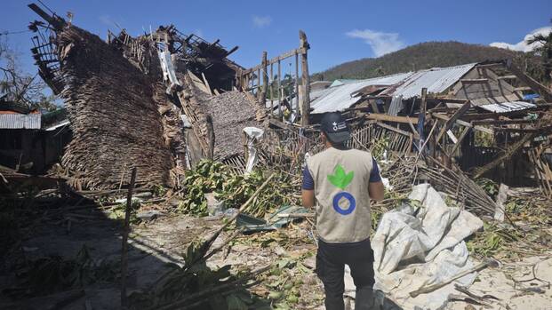 Mitarbeiter von Aktion gegen den Hunger vor zerstörten Häusern durch Taifun in Barangay Liberty, Hibisong Island, Loreto Dinagat Islands (Philippinen)