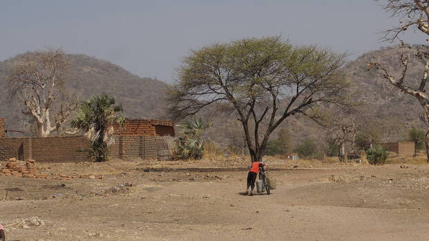 Eine Person schiebt ein Fahrrad in einer kargen ländlichen Umgebung in Süd-Kurdufan, Sudan.