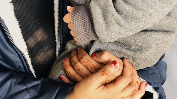 Aliya hält schützend die Hände um ihren Sohn. Eine Mutter hält schützend ihre Hände um ihr Kind.