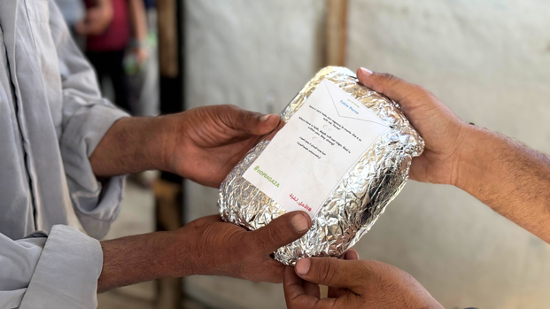 Ein Mitarbeiter von Aktion gegen den Hunger übergibt eine warme Mahlzeit, auf deren Packung eine Botschaft der Hoffnung steht.
