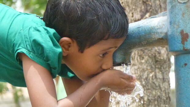 Kind trinkt Wasser aus einem Brunnen.