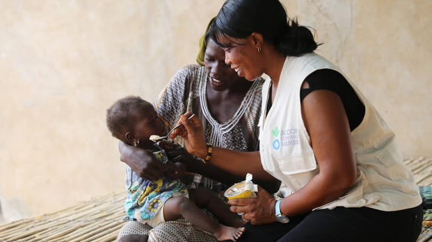 Helferin von Aktion gegen den Hunger füttert Kind mit einem Löffel.