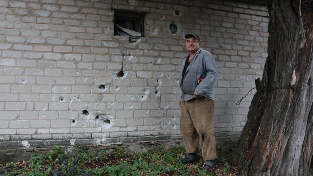 Ein Hilfeempfänger in der Ukraine steht vor einer zerschossenen Wand.