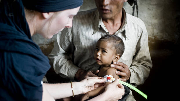 Kleines Kind bei der Messung seines Armumfangs mithilfe des MUAC-Bands. Diagnose: schwere Mangelernährung
