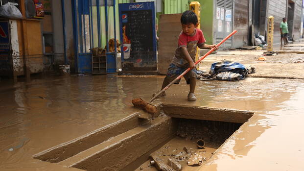 Kind fegt Wasser weg, nach starken Regenfällen in Peru